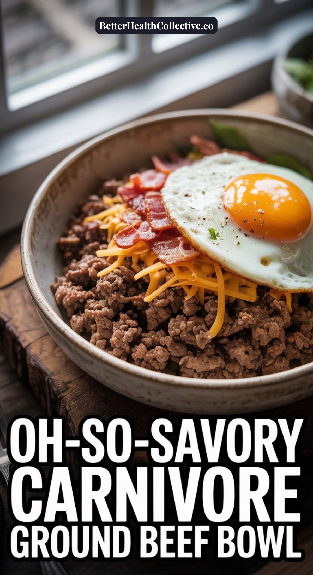 A bowl filled with ground beef, shredded cheddar cheese, crispy bacon pieces, and a sunny side up egg sits on a wooden surface by a window. Text reads: Oh-So-Savory Savory Carnivore Ground Beef Bowls.
