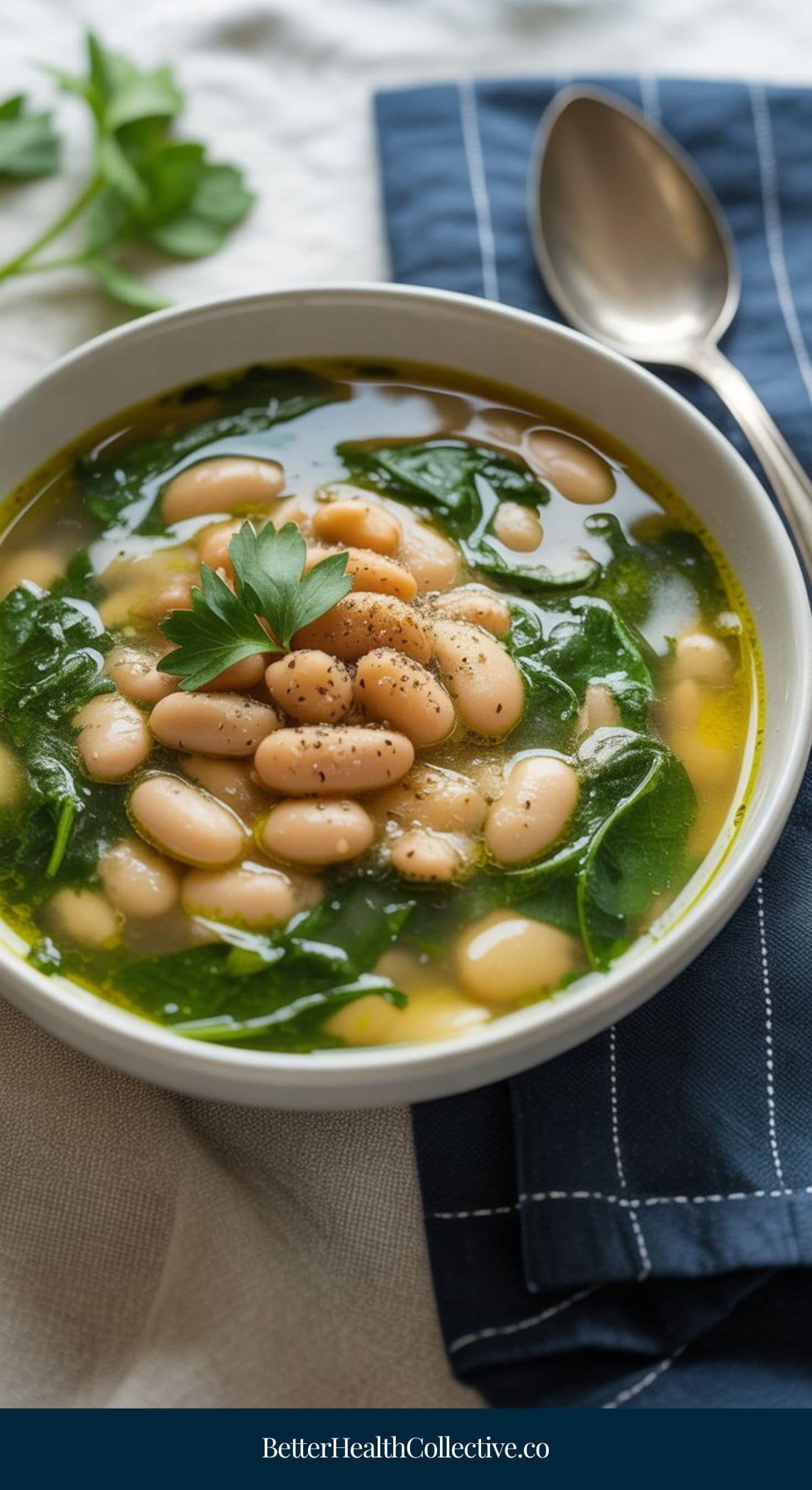 A bowl of white bean and spinach soup, a favorite among vegetarian soup recipes, garnished with fresh parsley and cracked black pepper, sits on a blue napkin with a spoon nearby.