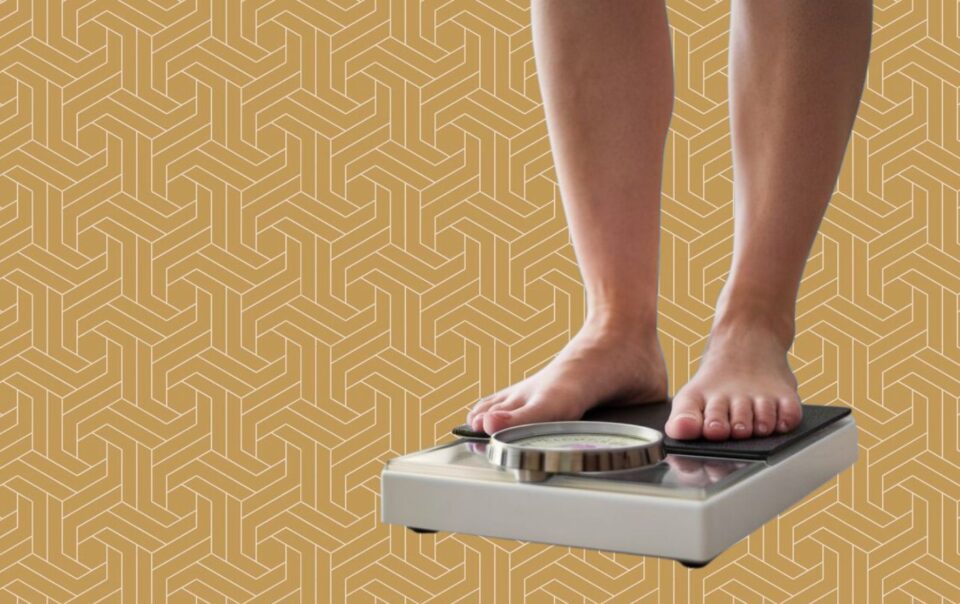 A person stands barefoot on a bathroom scale, symbolizing their fat loss journey, against a yellow geometric patterned background. The scale’s dial is visible, but the weight reading remains unclear.