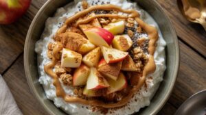 A delicious Apple Peanut Butter Cottage Cheese Bowl topped with apple slices, granola, chia seeds, and cinnamon, perfect as a high-protein breakfast or snack, set invitingly on a wooden table.