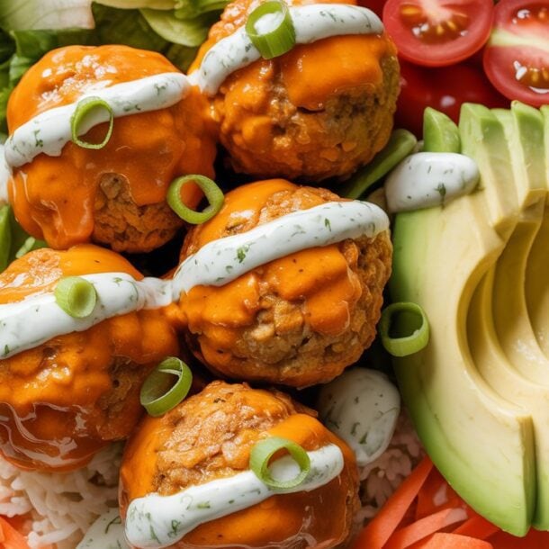 A Protein Bowl featuring rice, lettuce, shredded carrots, cherry tomato halves, avocado slices, and four saucy Buffalo Turkey Meatballs topped with creamy ranch dressing and sliced green onions.