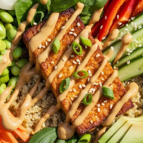 A vibrant Vegan Protein Bowl featuring quinoa, edamame, spinach, fresh veggies, avocado, and crispy tofu glazed to perfection—all topped with creamy sauce, green onions, and sesame seeds. Ideal for high-protein meal prep.