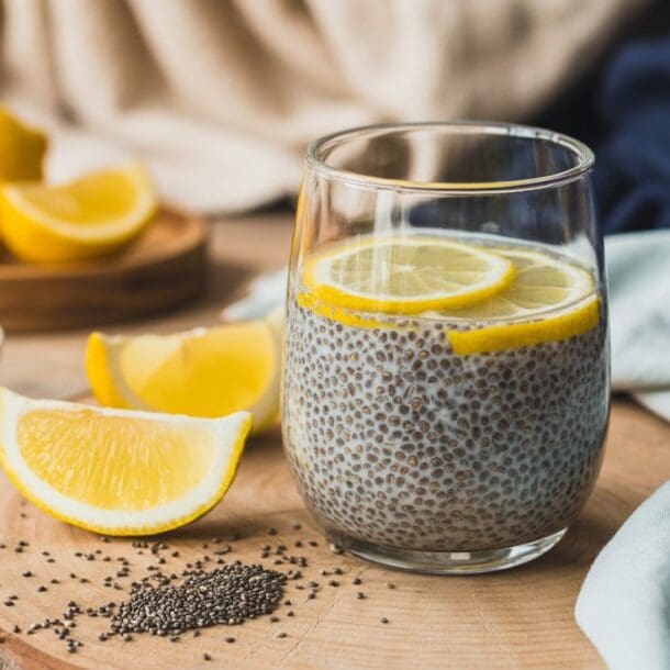A glass of chia seed pudding garnished with lemon slices sits on a wooden board with lemon wedges, a small bowl of chia seeds, and a cloth napkin nearby—perfect as part of a science-backed Natural Ozempic drink recipe.