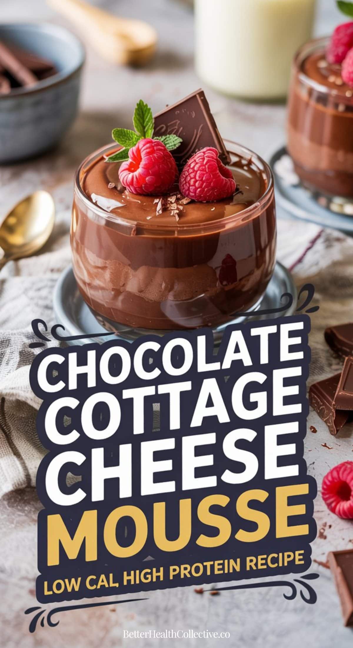 A glass bowl of high-protein cottage cheese chocolate mousse topped with raspberries and mint sits on a table. A gold spoon, chocolate pieces, and another mousse bowl are nearby. Text on image: Chocolate Cottage Cheese Mousse.