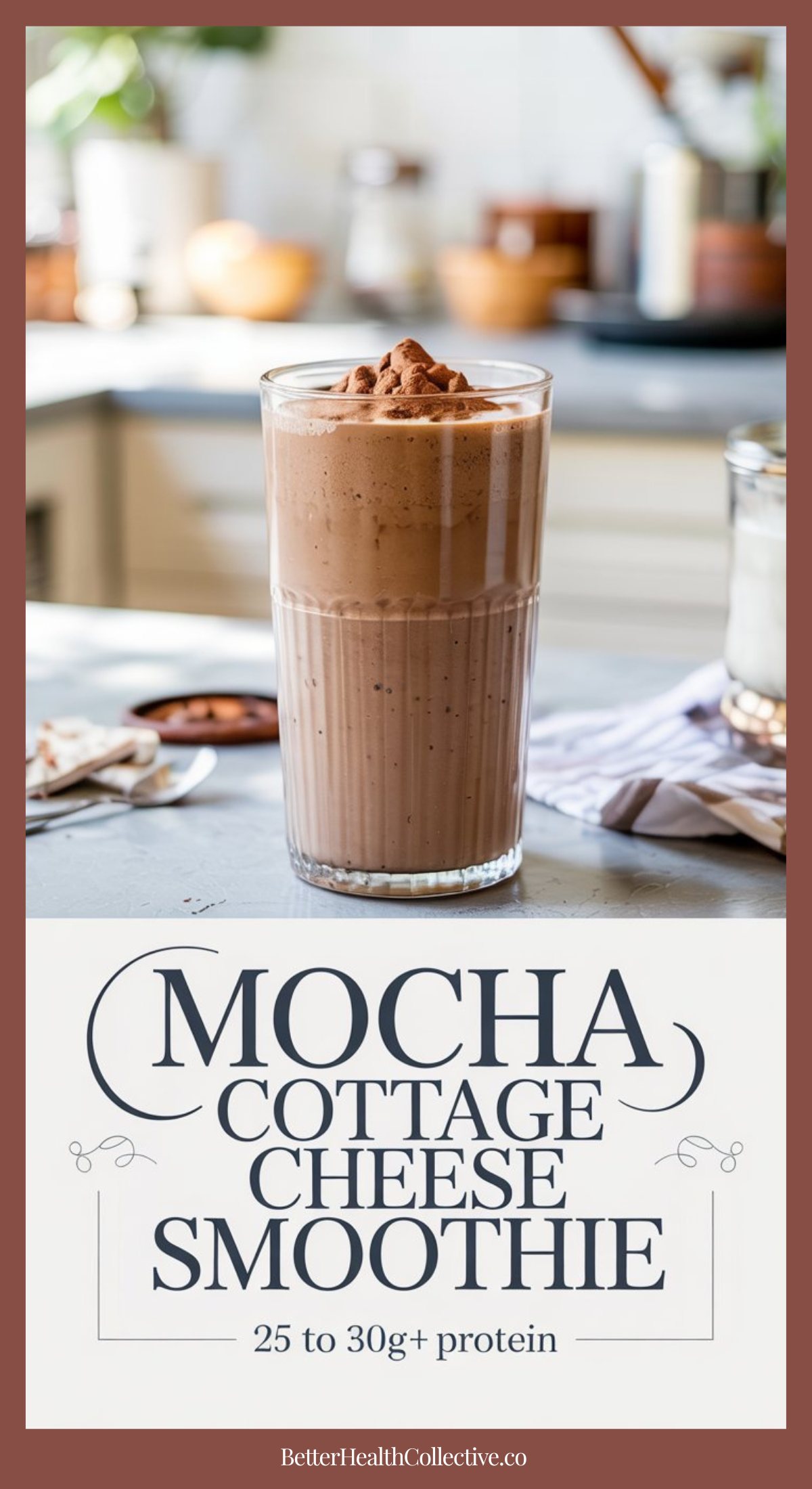 A tall glass of Mocha Cottage Cheese Smoothie sits on a kitchen counter, topped with cocoa powder. Text below reads, Mocha Cottage Cheese Smoothie, 25 to 30g+ protein. The softly blurred kitchen background adds a cozy touch.