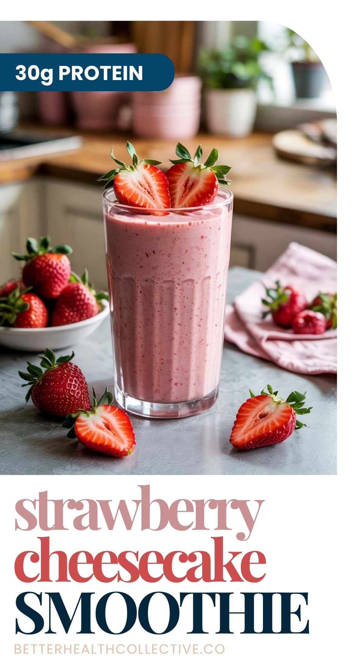 A glass of Strawberry Cheesecake Cottage Cheese Smoothie topped with fresh strawberries sits on a kitchen counter, surrounded by whole strawberries and a pink napkin. Text reads: “30g protein. Strawberry cheesecake smoothie.”.