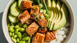 A vibrant rice bowl featuring teriyaki salmon cubes, avocado, cucumber, edamame, green onions, and sesame seeds—perfect for meal prep or a delicious lunch.