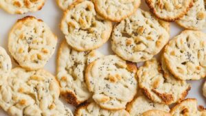A close-up view of several crispy, golden-brown, round cookies with a slightly uneven surface and sprinkled seeds, arranged on a white background—perfect as a high-protein snack.