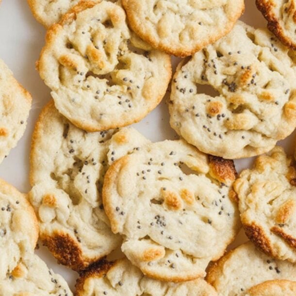 A close-up view of several crispy, golden-brown, round cookies with a slightly uneven surface and sprinkled seeds, arranged on a white background—perfect as a high-protein snack.