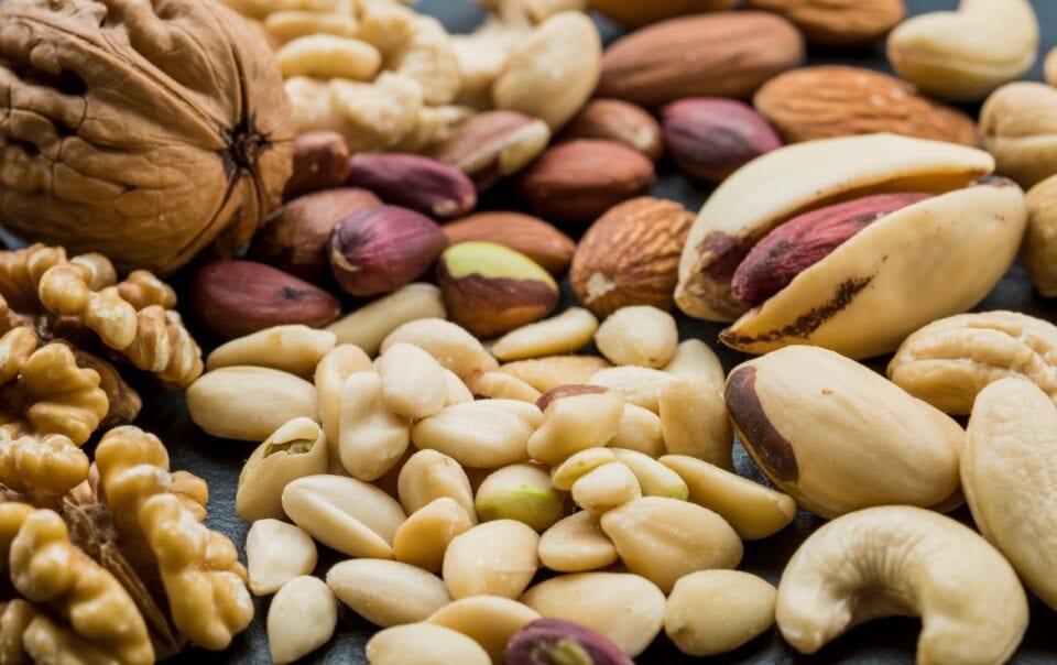 A close-up of assorted healthy nuts, including walnuts, almonds, cashews, pistachios, and peanuts, arranged together on a dark surface.